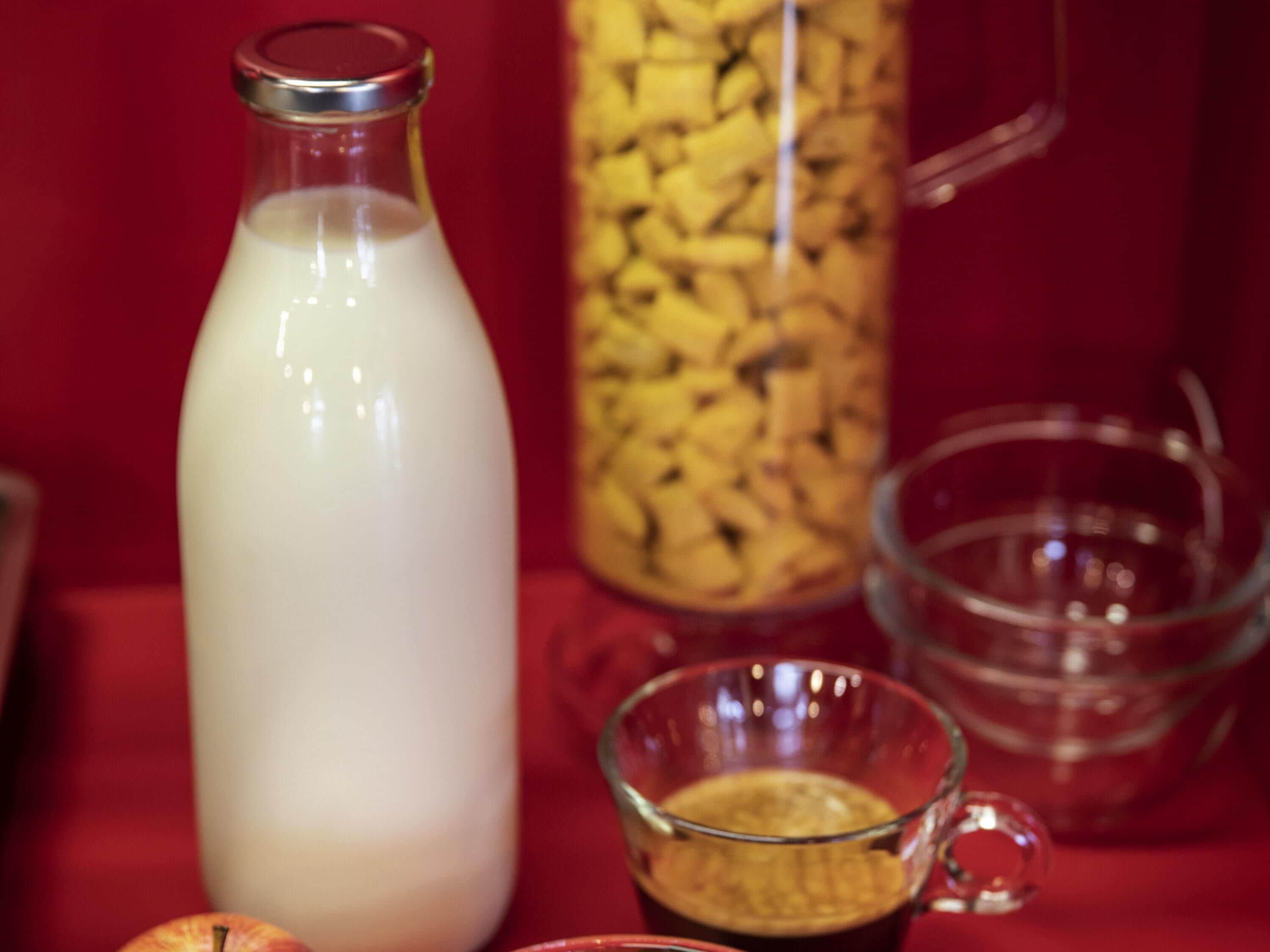 Eine Milchflasche, eine Tasse mit einem Getränk und eine Karaffe auf roter Oberfläche.