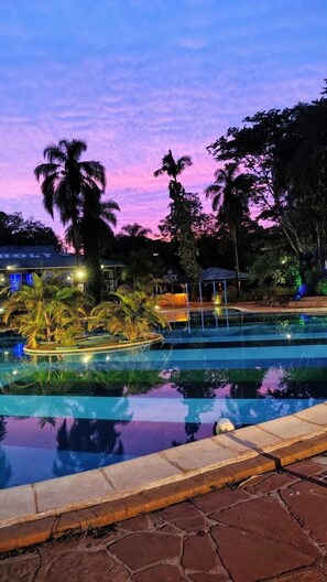 A swimming pool with a stone border, surrounded by palm trees and a building with 'HOLY' written on it. - Beer Hotel Iguazu - Hostel (Puerto Iguazú)