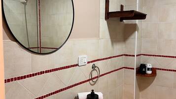 Un baño con tocador de madera, un espejo redondo, un lavamanos y zona de ducha.