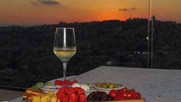 Una mesa con una copa de vino blanco y una tabla de madera con frutas y verduras variadas.
