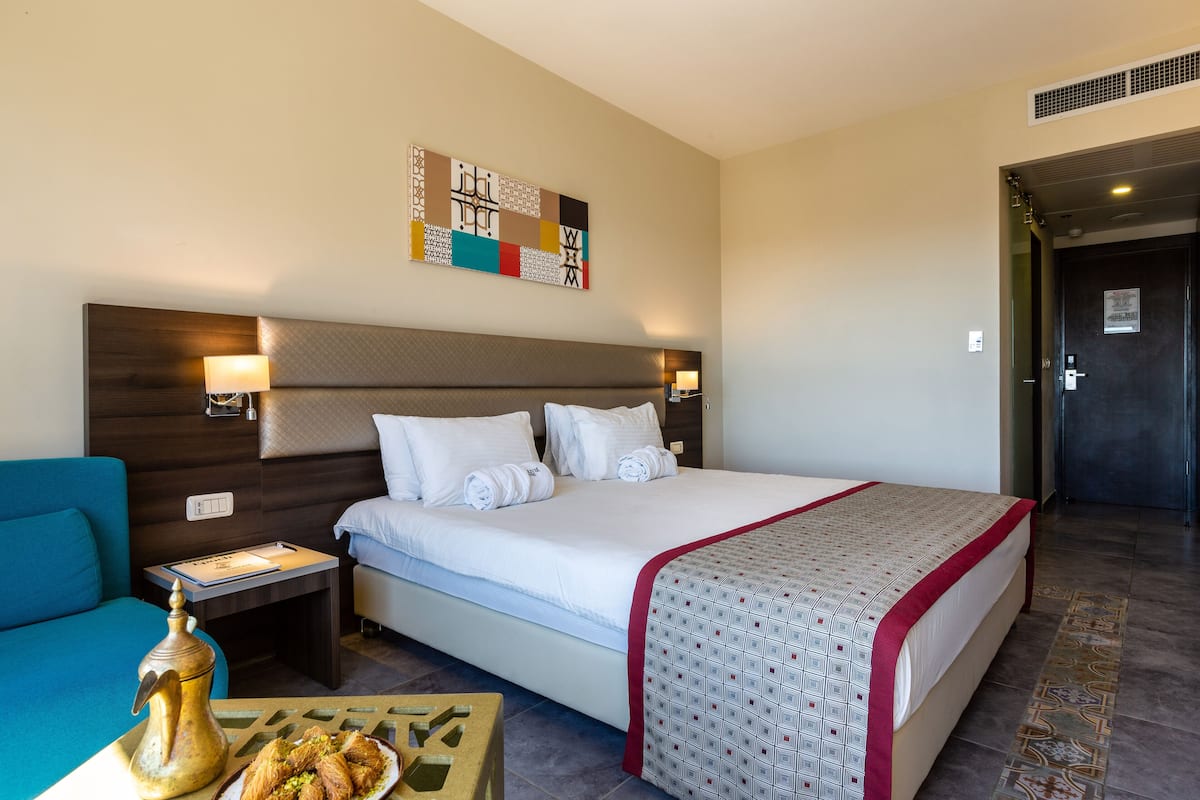 Ein Hotelzimmer mit einem großen Bett, einem Nachttisch mit Lampe, einem kleinen Tisch mit Dekoration und einem Wandbild.