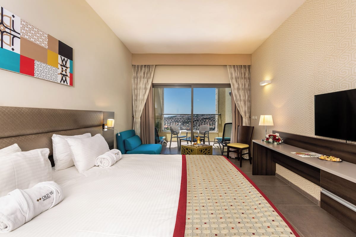 Ein Hotelzimmer mit einem großen Bett, einem Schreibtisch, einem Fernseher und einem Balkon mit Blick.