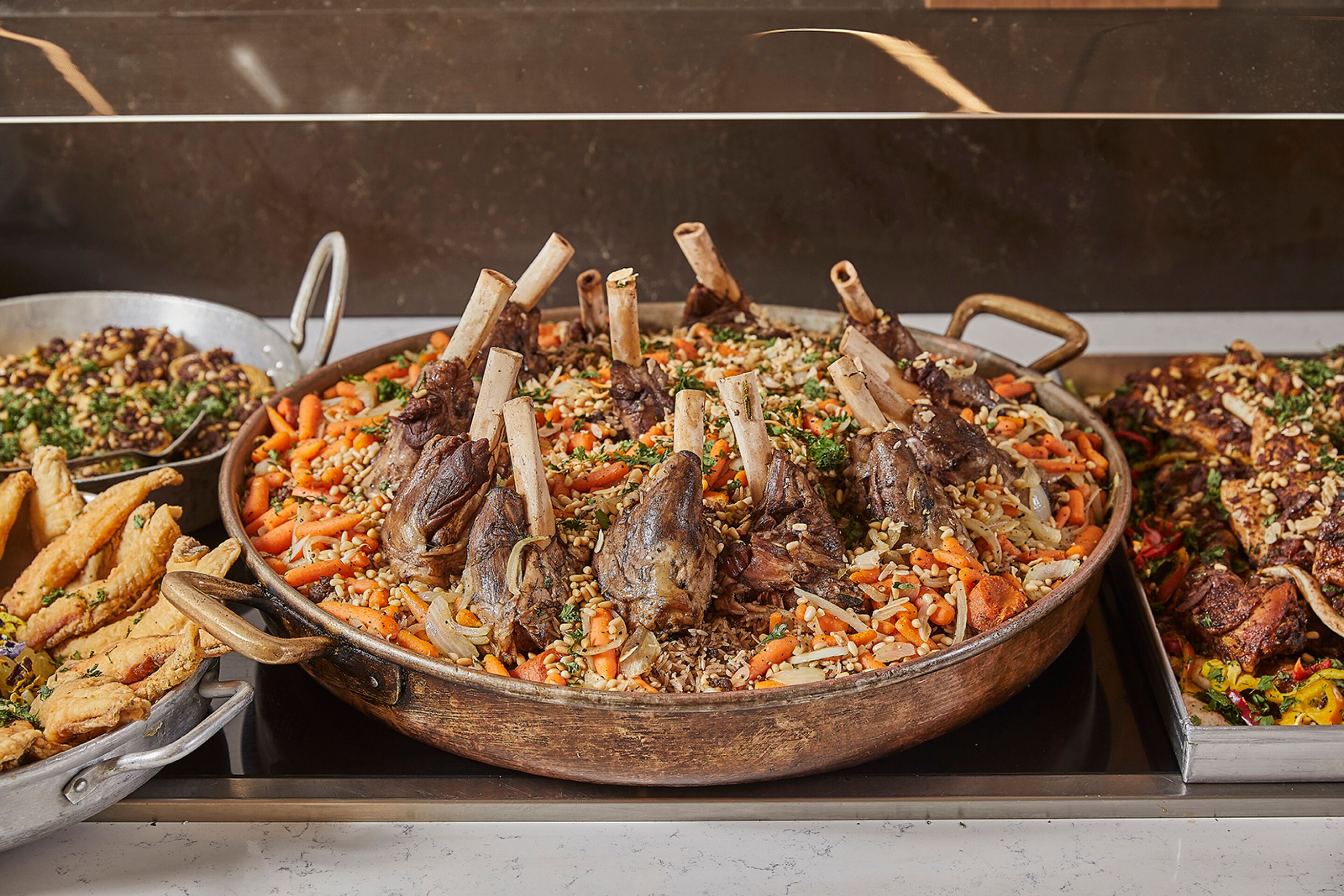 A large wooden serving dish filled with a dish of meat and vegetables, surrounded by other dishes.