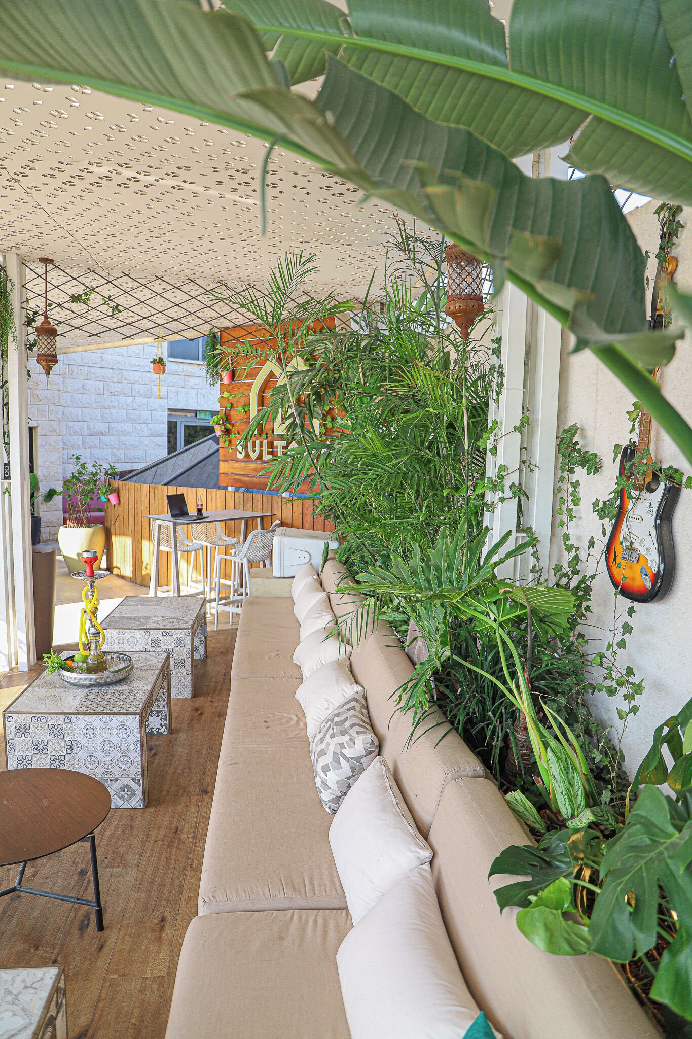 A cozy outdoor seating area with a sofa, chairs, and a table, surrounded by lush plants and a guitar on the wall.