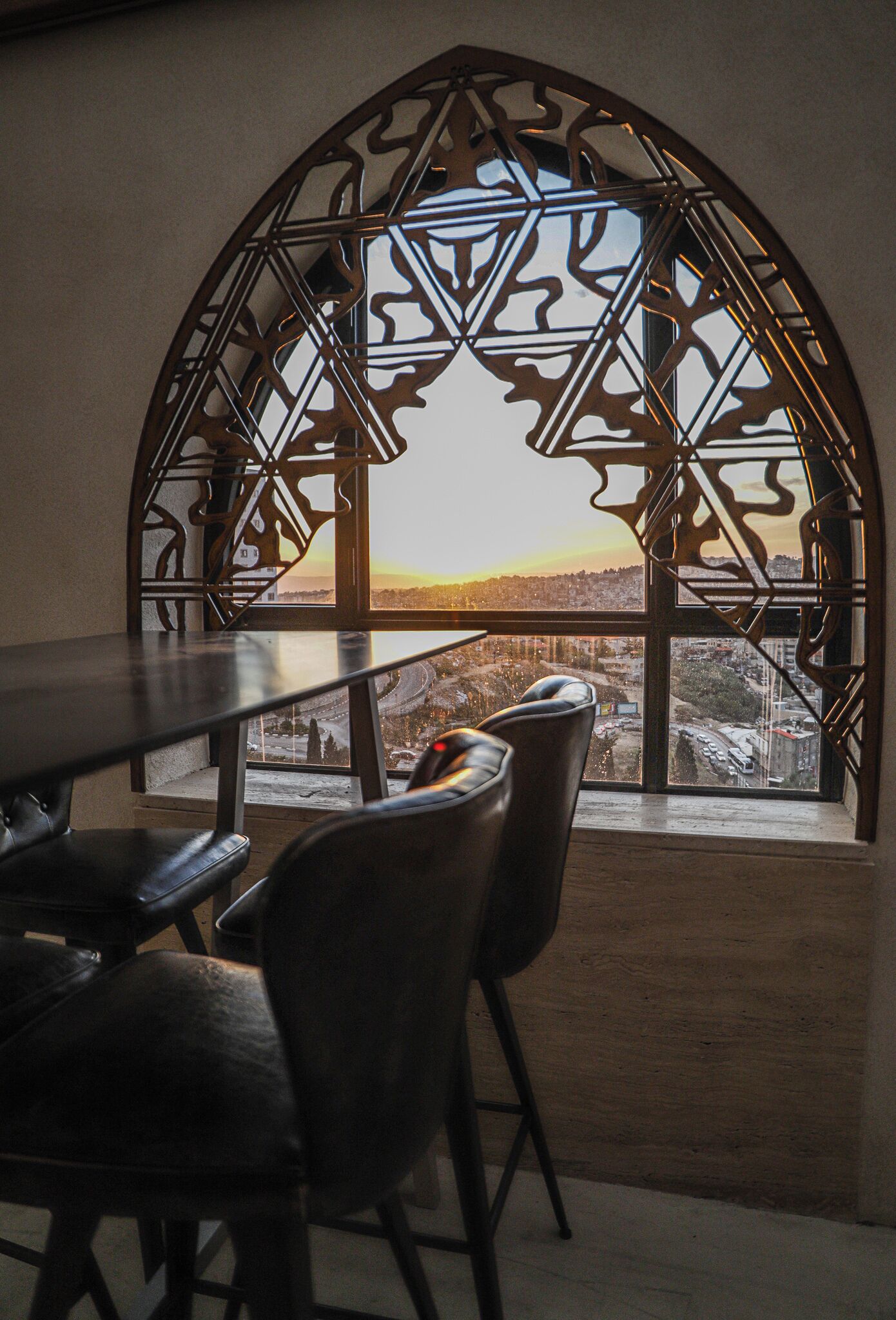 Un área de comedor con una mesa y sillas, un marco de ventana decorativo y vista a un paisaje urbano.