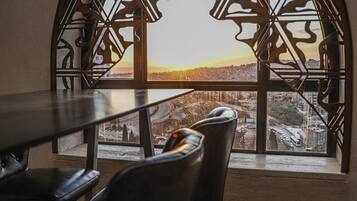Un área de comedor con una mesa y sillas, un marco de ventana decorativo y vista a un paisaje urbano.