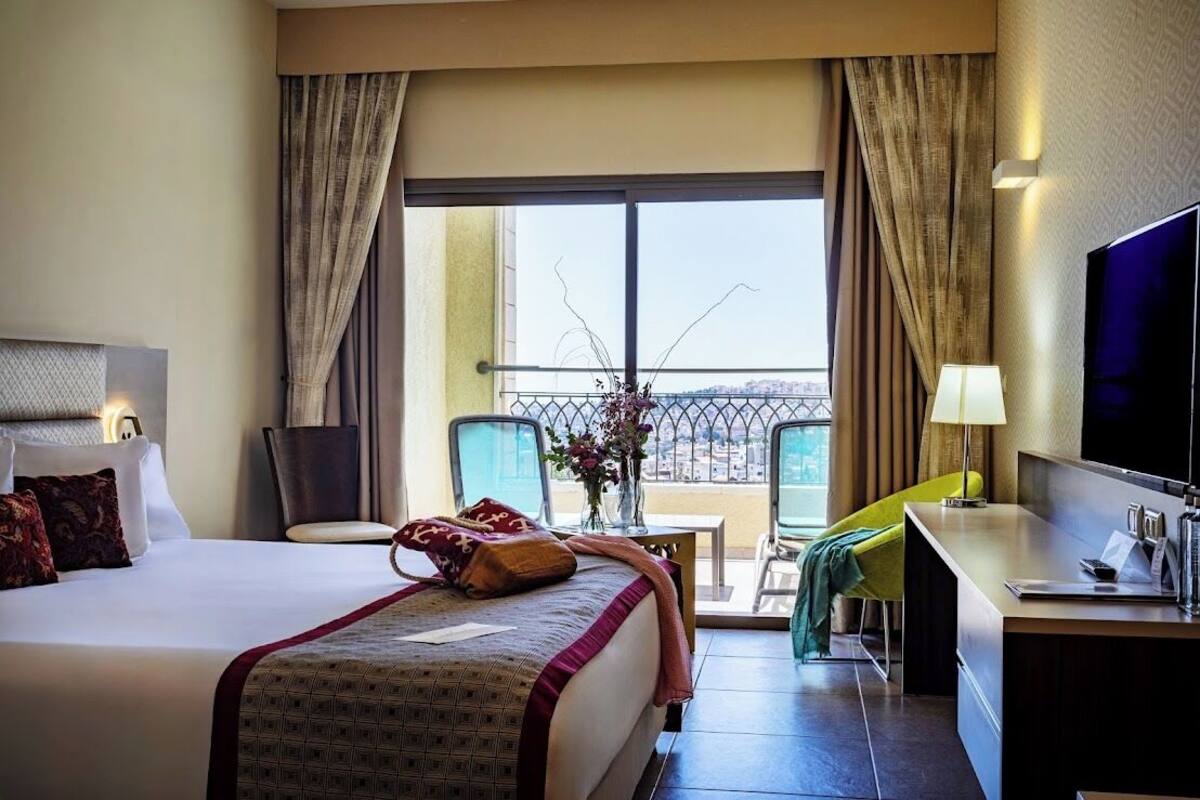 Ein Hotelzimmer mit einem großen Bett, einem Schreibtisch mit Stuhl, einem Fernseher und einem Balkon mit Blick.