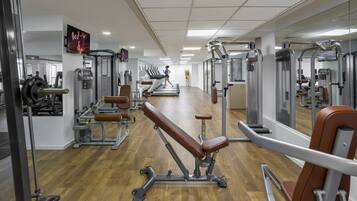 Ett gym med konditionsmaskiner, styrketräningsutrustning och en vägg med speglar.