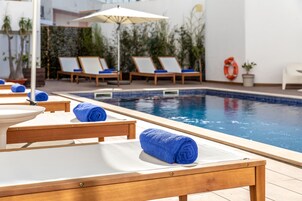 Zona de piscina con sillones de descanso y toallas, una piscina y un flotador.