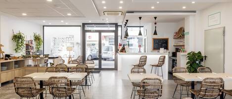 Un café moderno con muebles de mimbre, una barra central y vista a la calle.