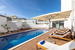 Zona de piscina en la azotea con sillones, sombrillas y un cielo azul despejado.