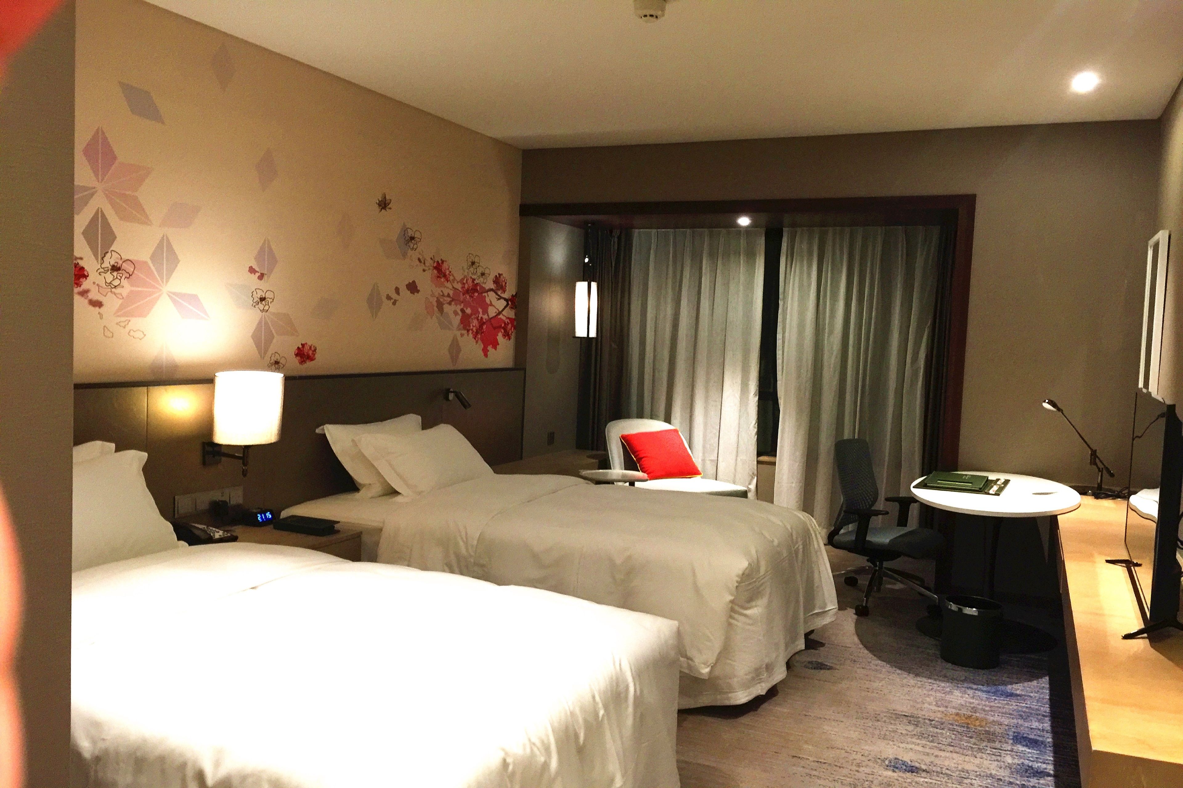 Una habitación de hotel con dos camas, un escritorio, una silla y una lámpara.