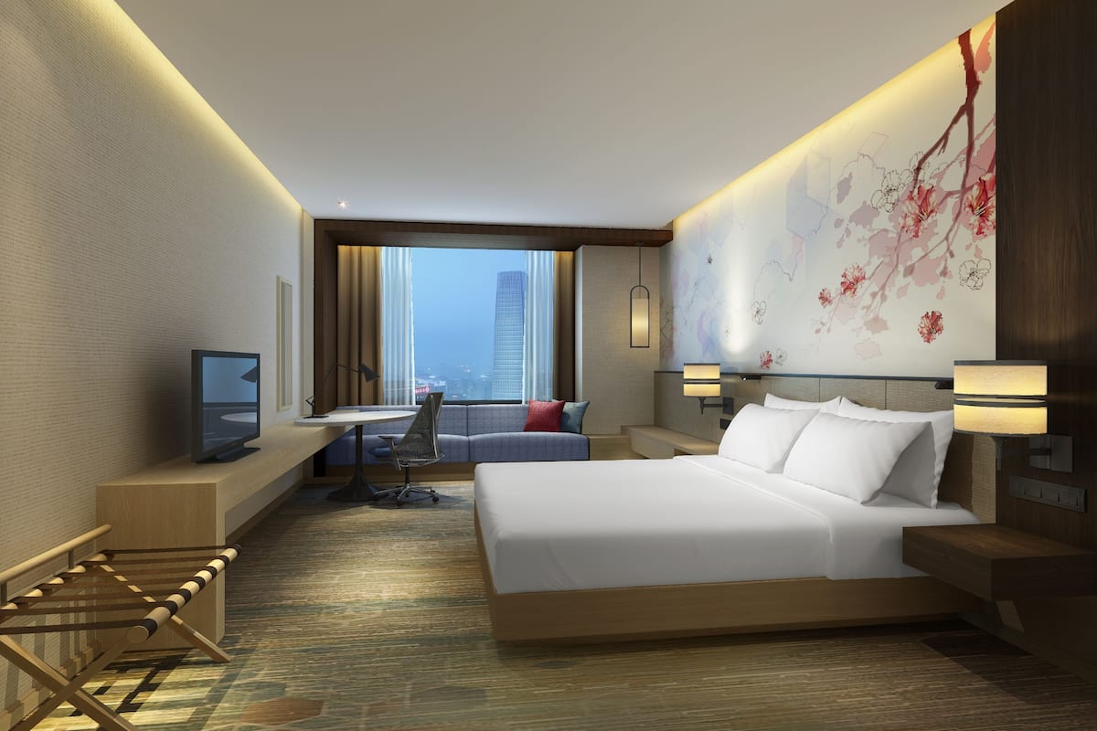 A modern hotel room with a large bed, a desk, a chair, and a TV.
