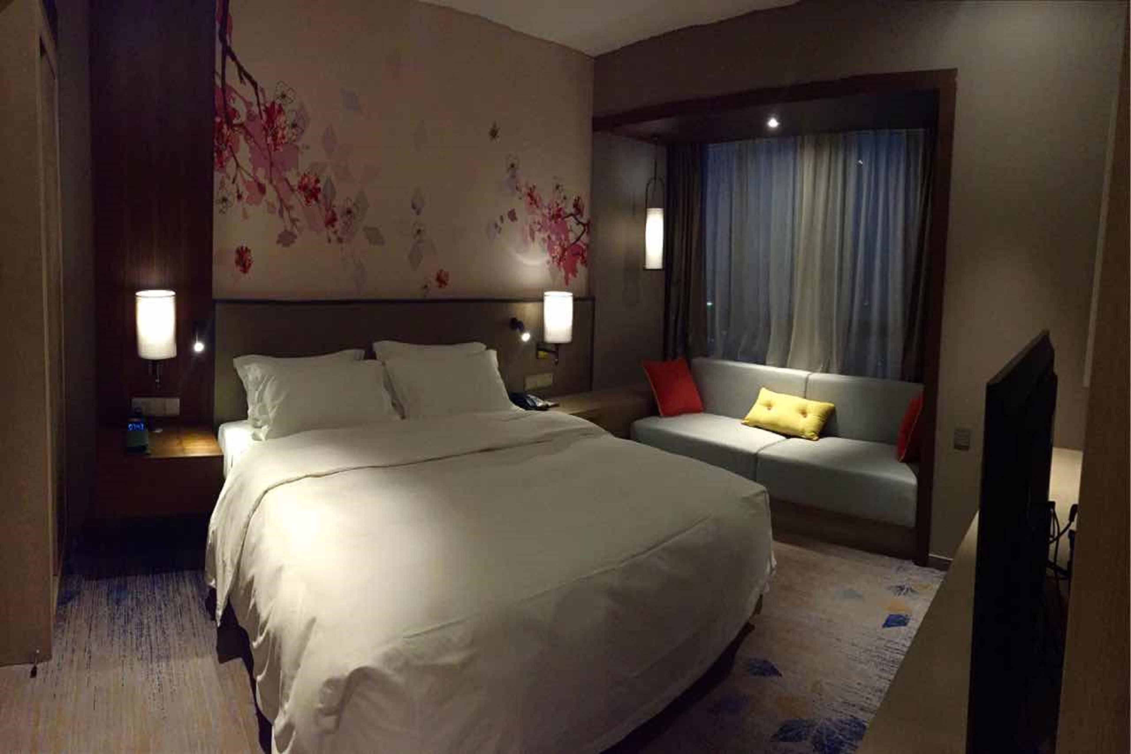 A hotel room with a large bed, a sofa, a TV, and a window with curtains.