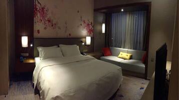 Una habitación de hotel con una cama grande, un sofá, un televisor y una ventana con cortinas.