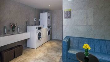 A modern bathroom with a built-in washing machine, a sink with a vase of flowers, and a blue sofa with a table.