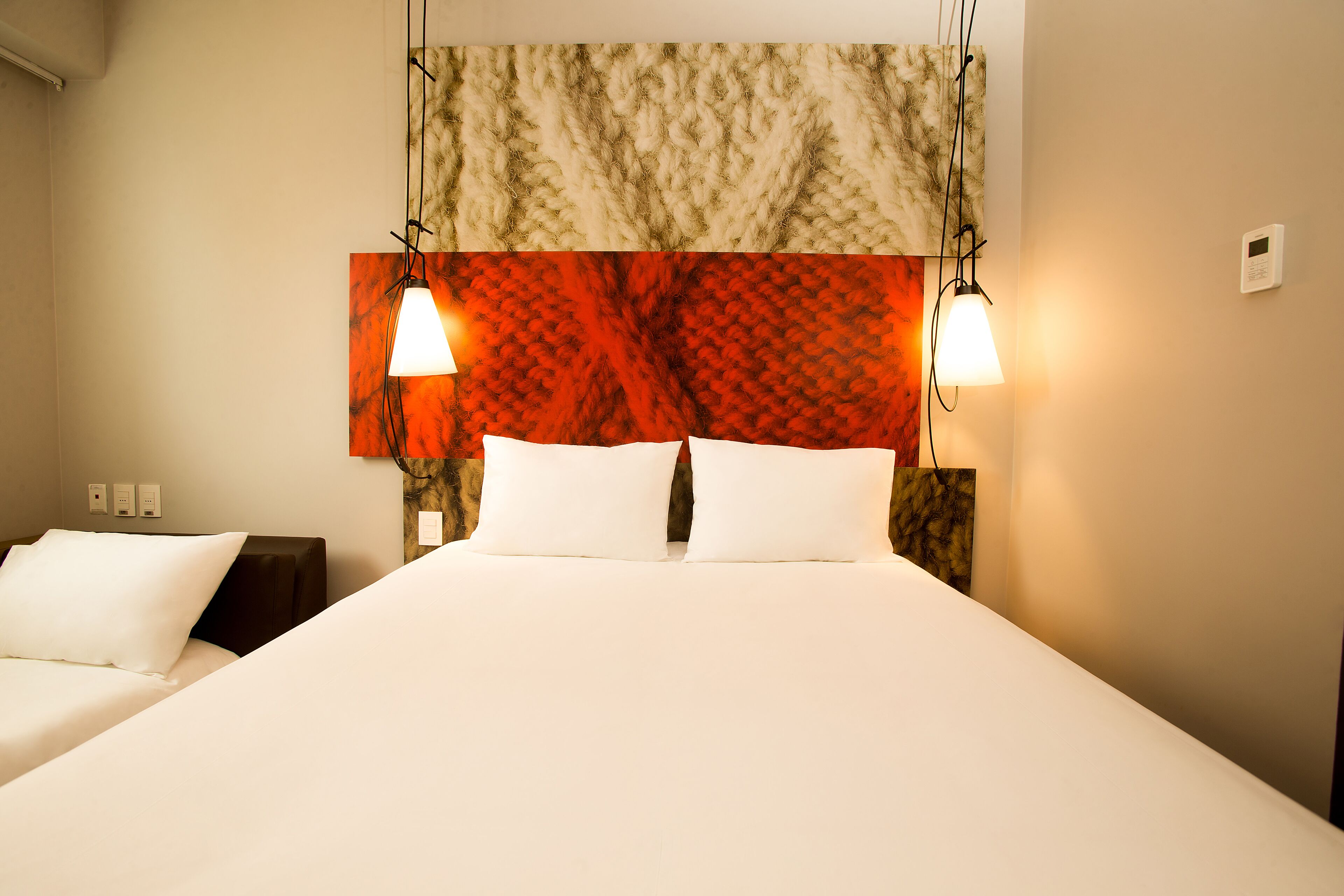 Quarto de hotel com uma cama grande, duas mesas de cabeceira e cabeceira com padrão decorativo.