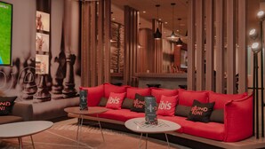 Een moderne lounge met een rode bank, twee kleine tafels en een groot scherm waarop een sportevenement wordt vertoond.