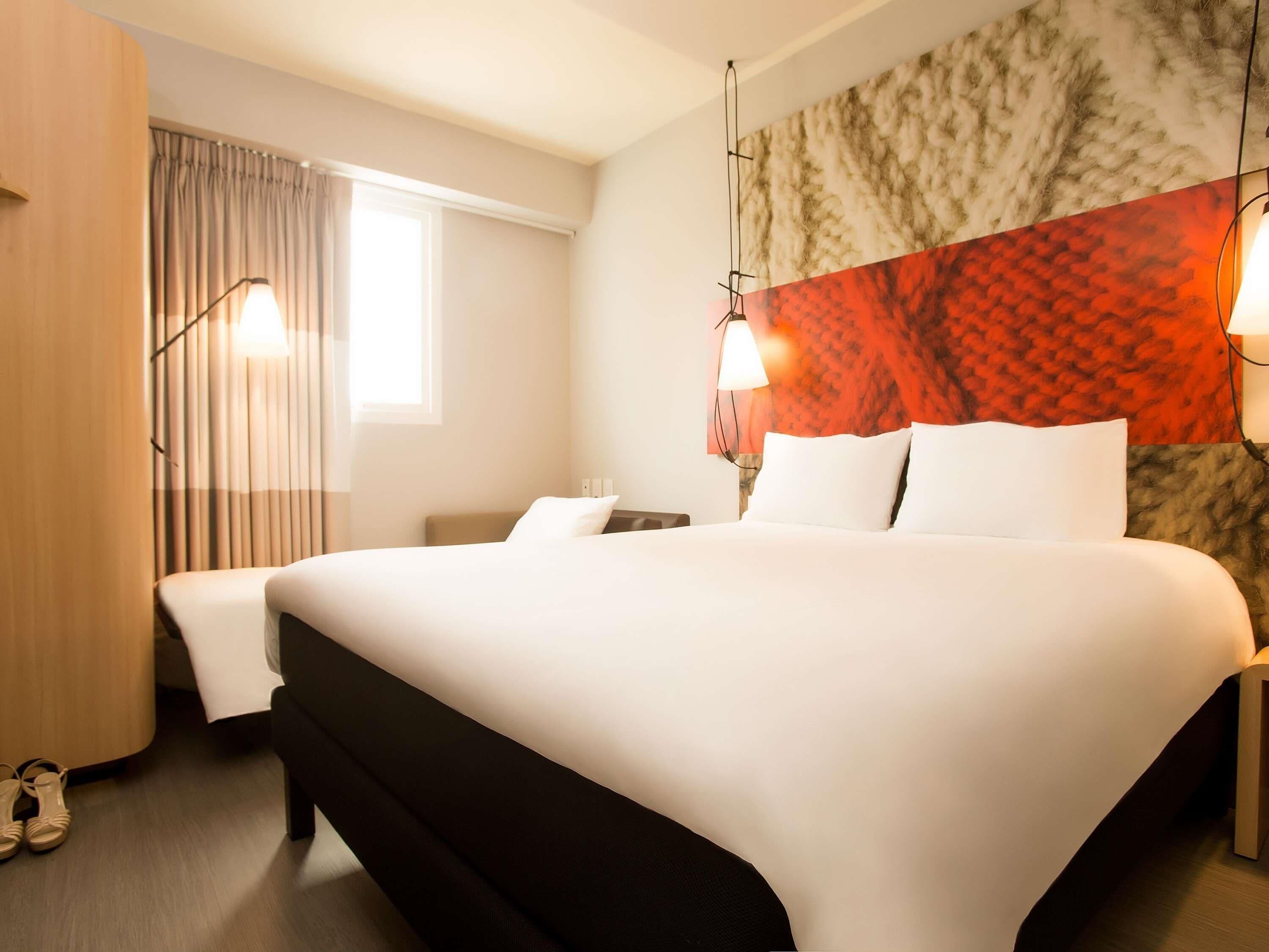 Een hotelkamer met een groot bed, een bureau, een stoel, een lamp en een raam met gordijnen.