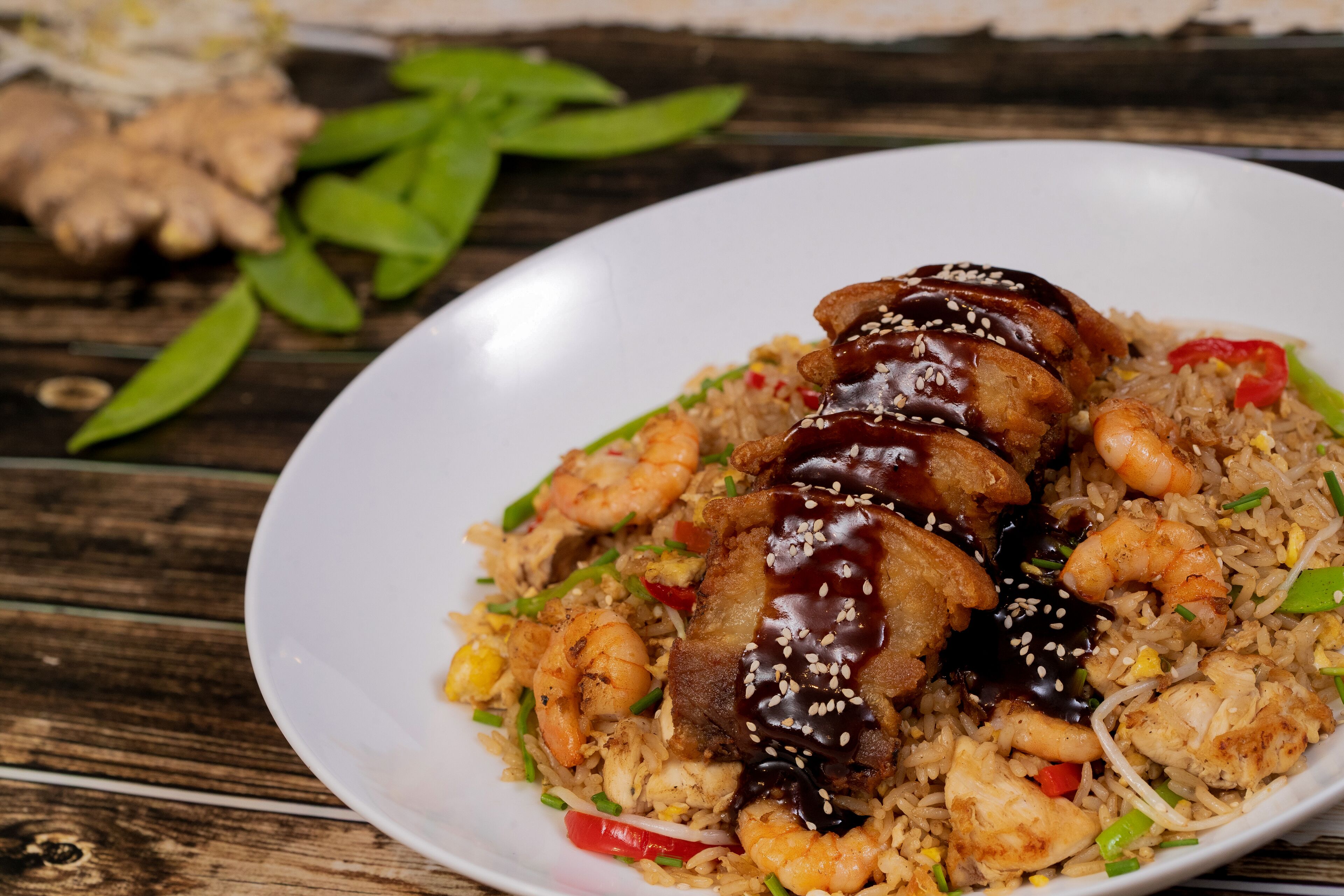 Une assiette de riz frit aux crevettes et au poulet, garnie de graines de sésame et d’une sauce foncée.
