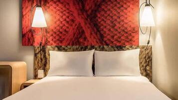 Una habitación de hotel con una cama grande, dos lámparas de noche y un cabecero con un diseño rojo estampado.