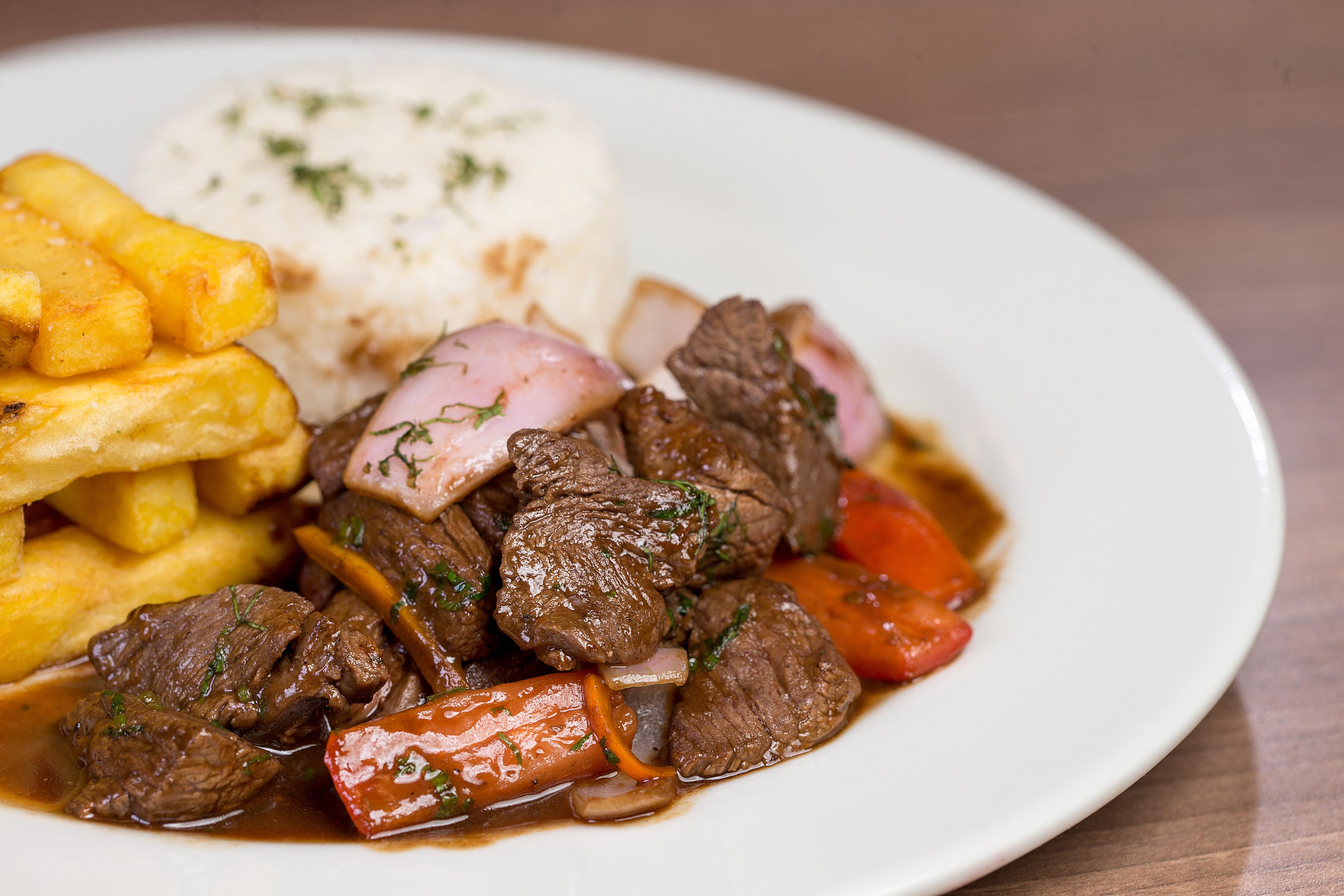 A plate of beef stew with vegetables and fries, served with a side of rice.