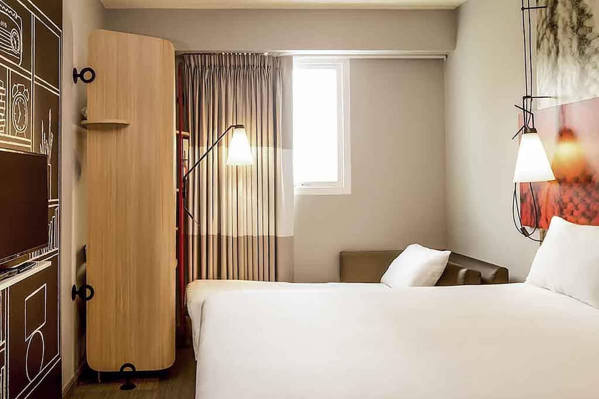 Ein Hotelzimmer mit Bett, Schrank, Schreibtisch und einem Fenster mit Vorhängen.