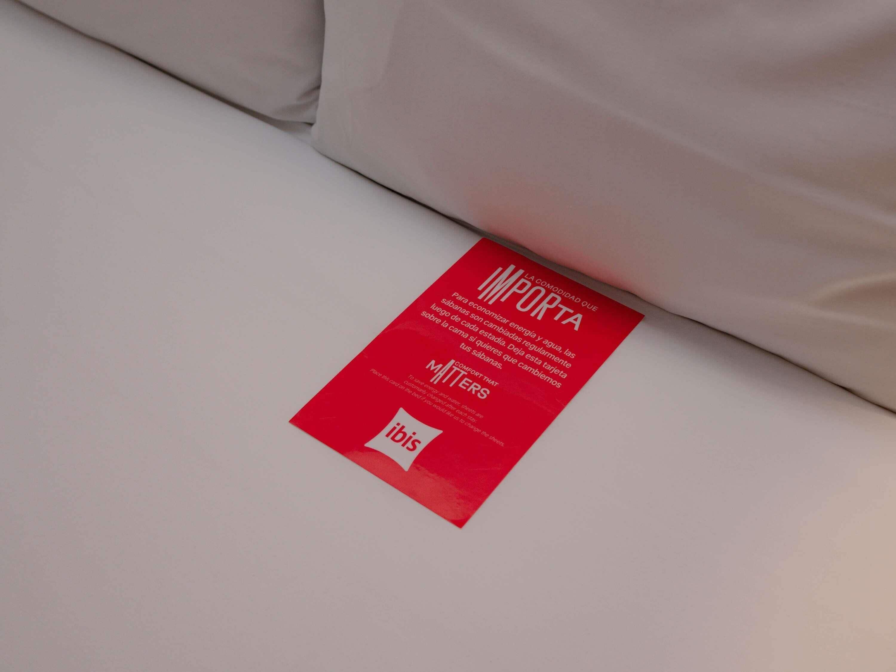 A red informational card on a bed with text in Spanish.
