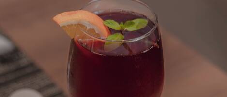 Un vaso de bebida roja con una rodaja de naranja y hojas de menta sobre una mesa de madera.