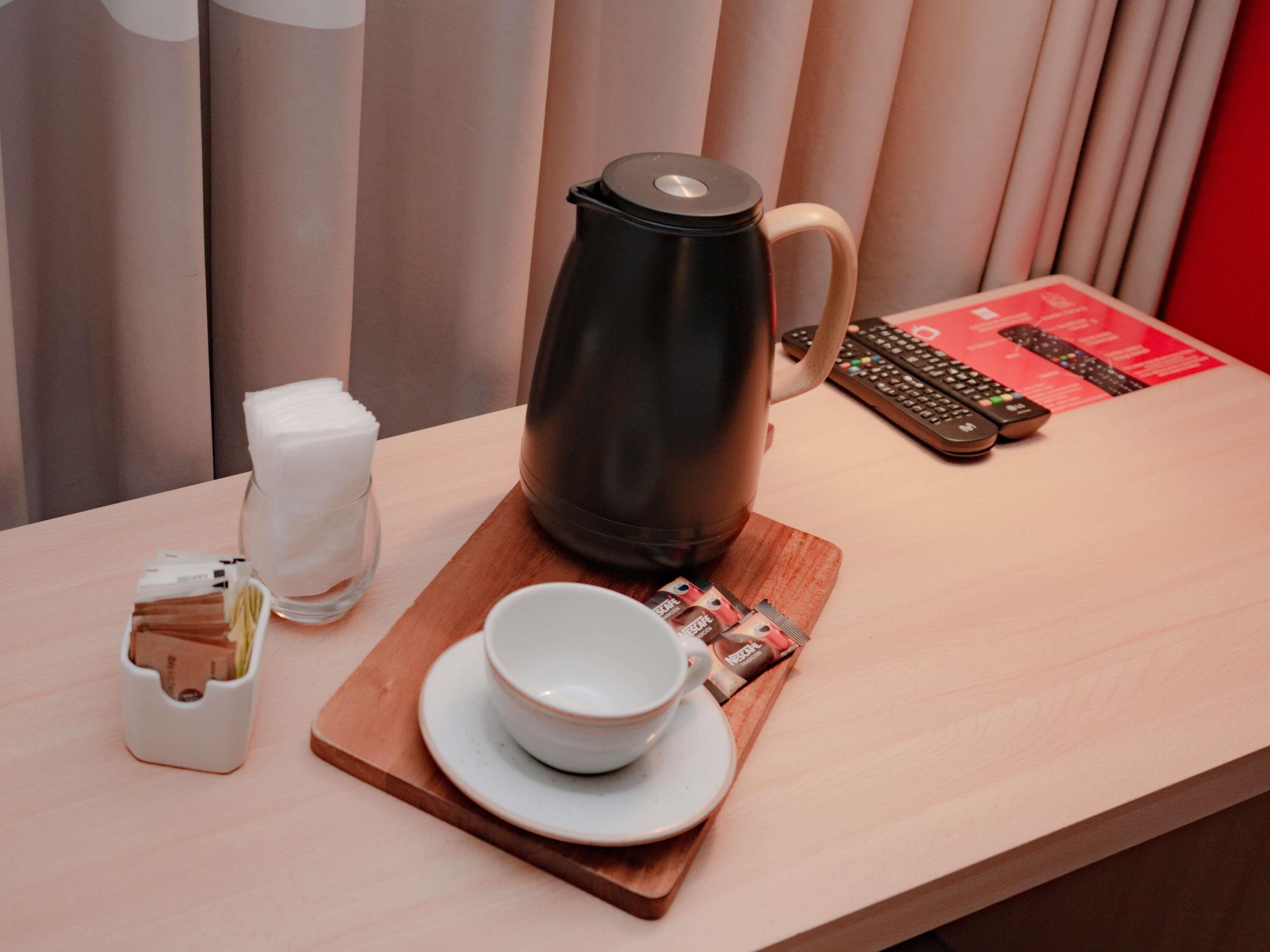 A coffee maker, a cup, a remote control, and a tray with coffee pods on a wooden table.
