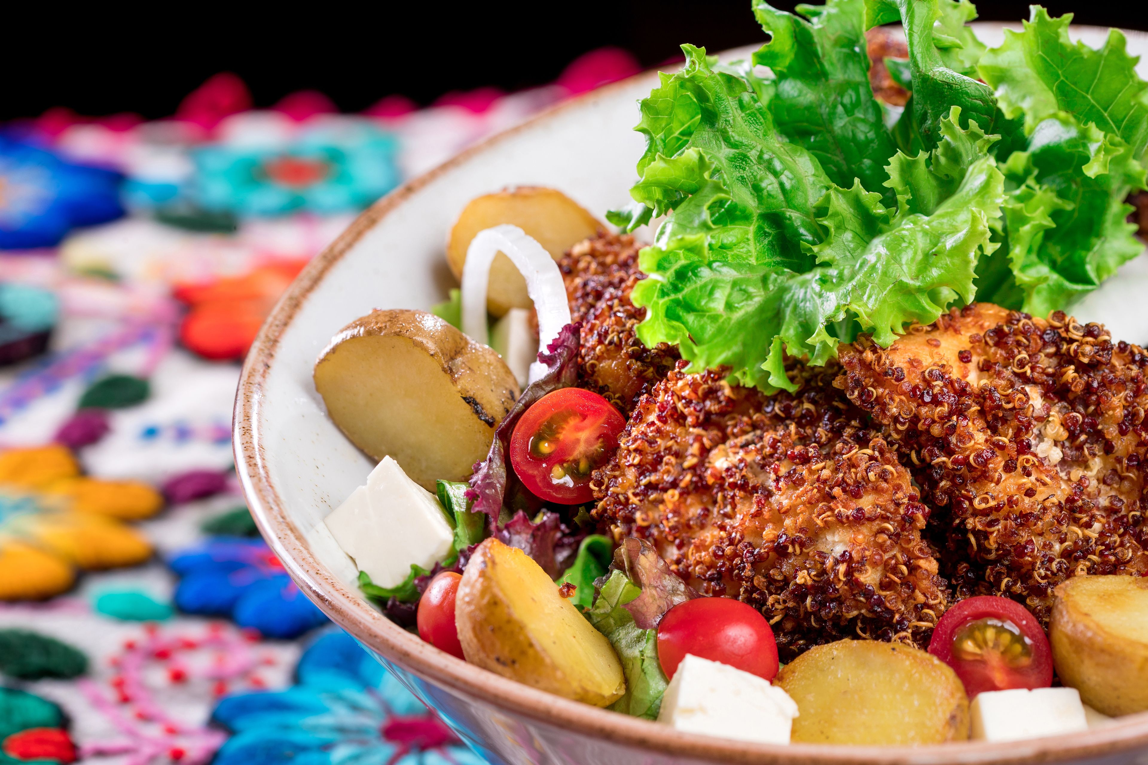 A bowl of food with various items including potatoes, lettuce, and a breaded chicken piece.