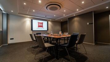 A conference room with a large table, chairs, a projector screen displaying 'ibis', and a carpeted floor.