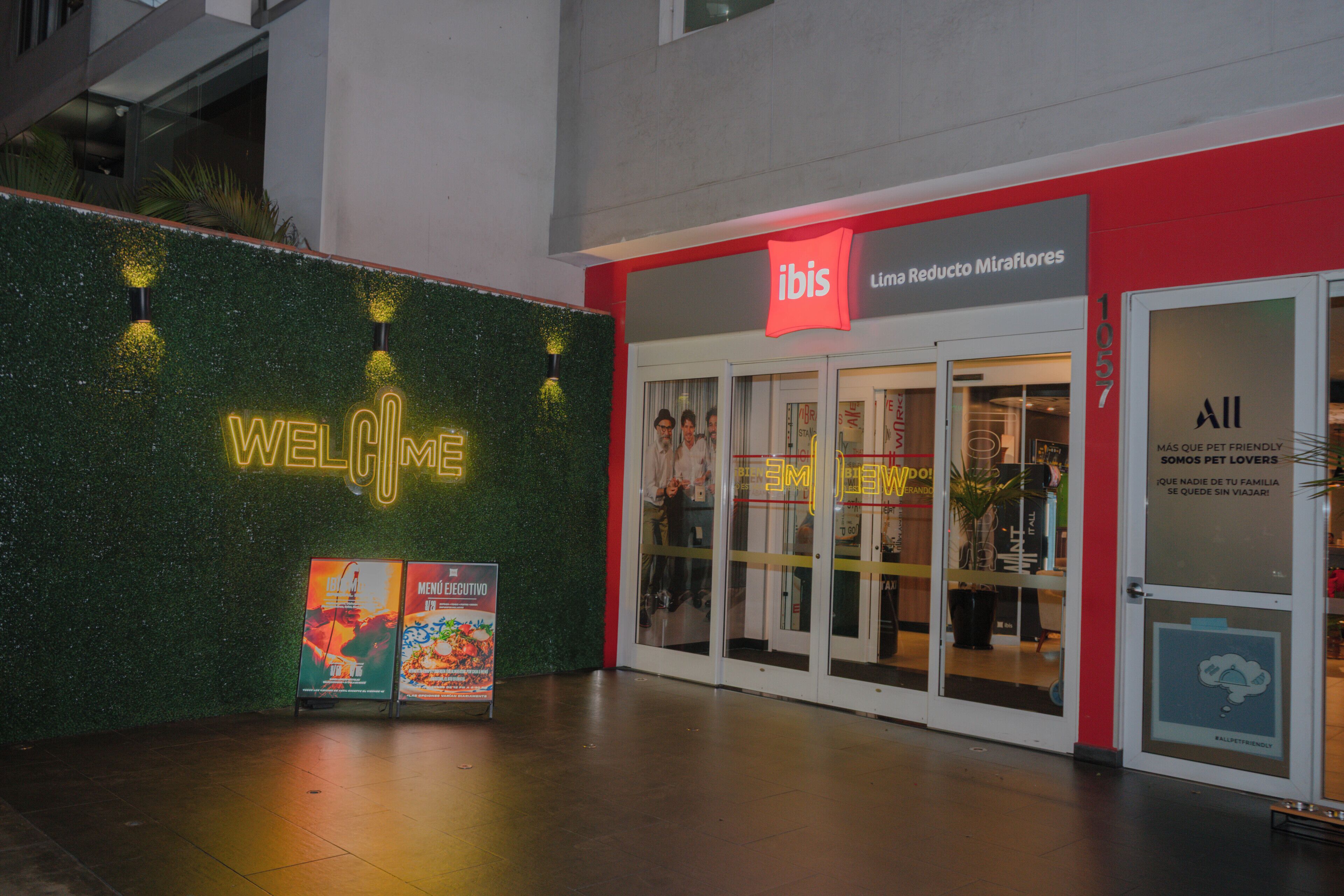 Entrada de hotel con un cartel de 'Welcome', un cartel de 'Limba Reducto MiraFlore' y un cartel que dice 'Somos amantes de las mascotas'.
