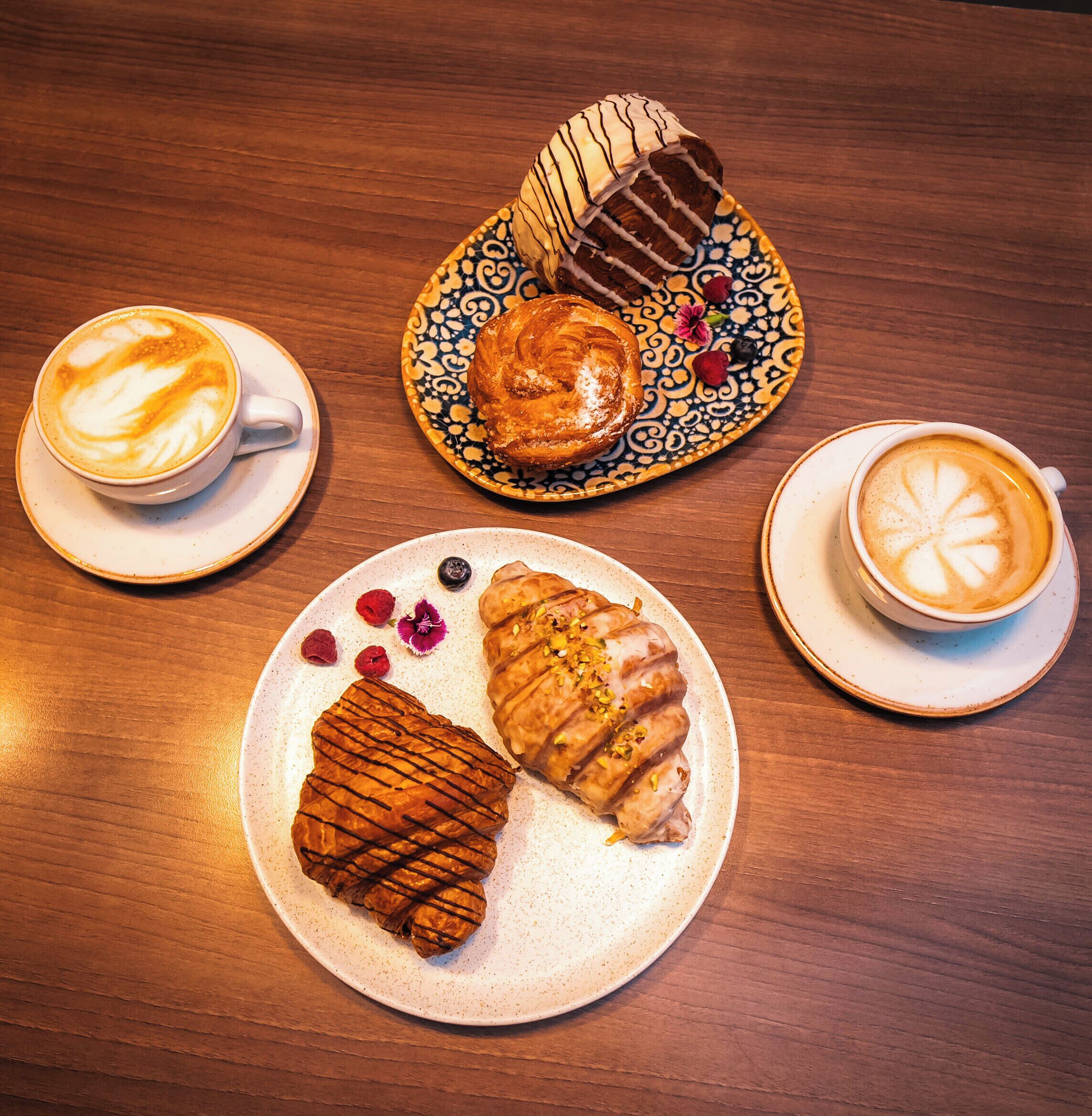 Una mesa con tres platos de pasteles y dos tazas de café.