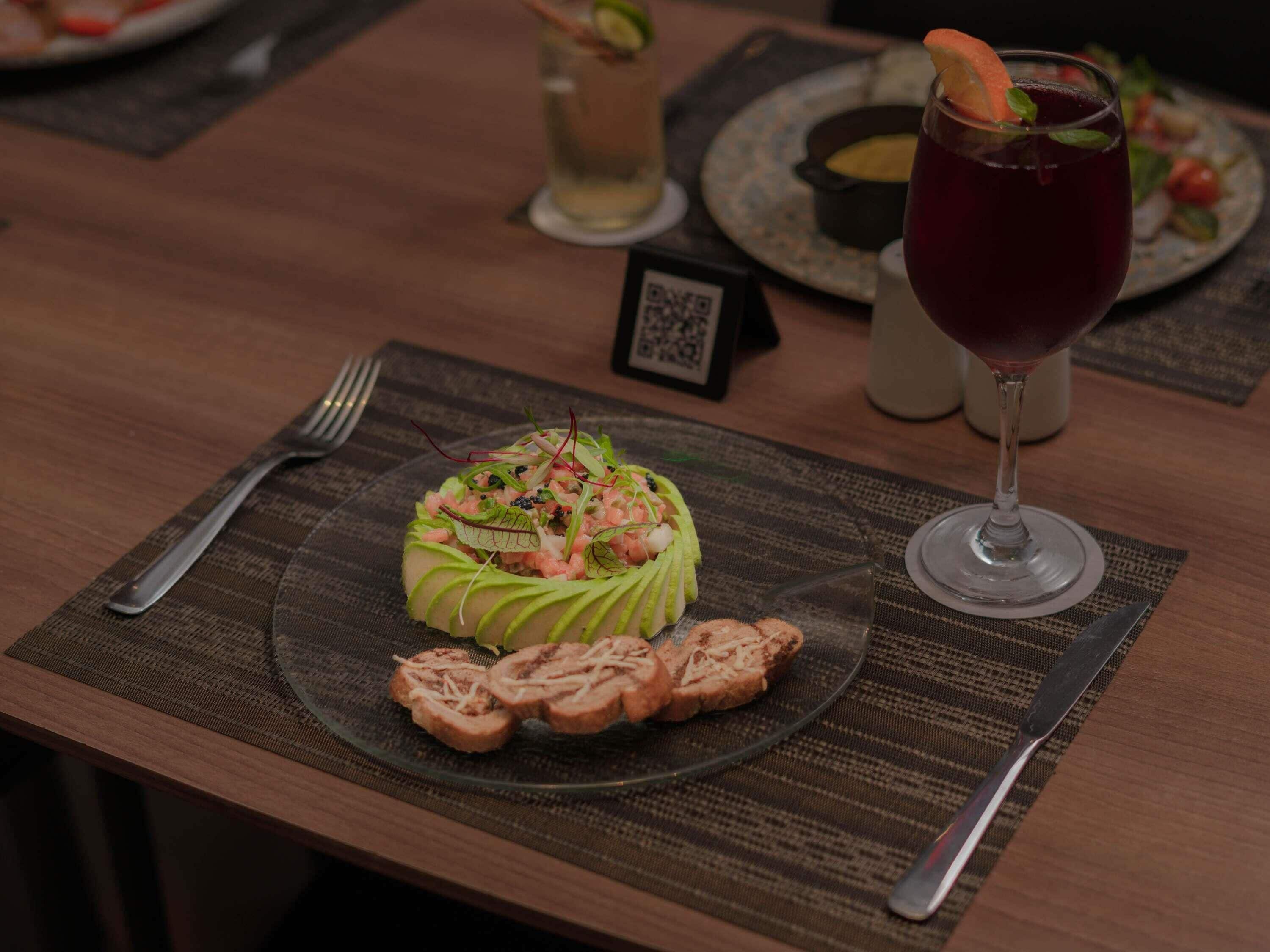 A dining table with a plate of food, a glass of red beverage, and a fork.