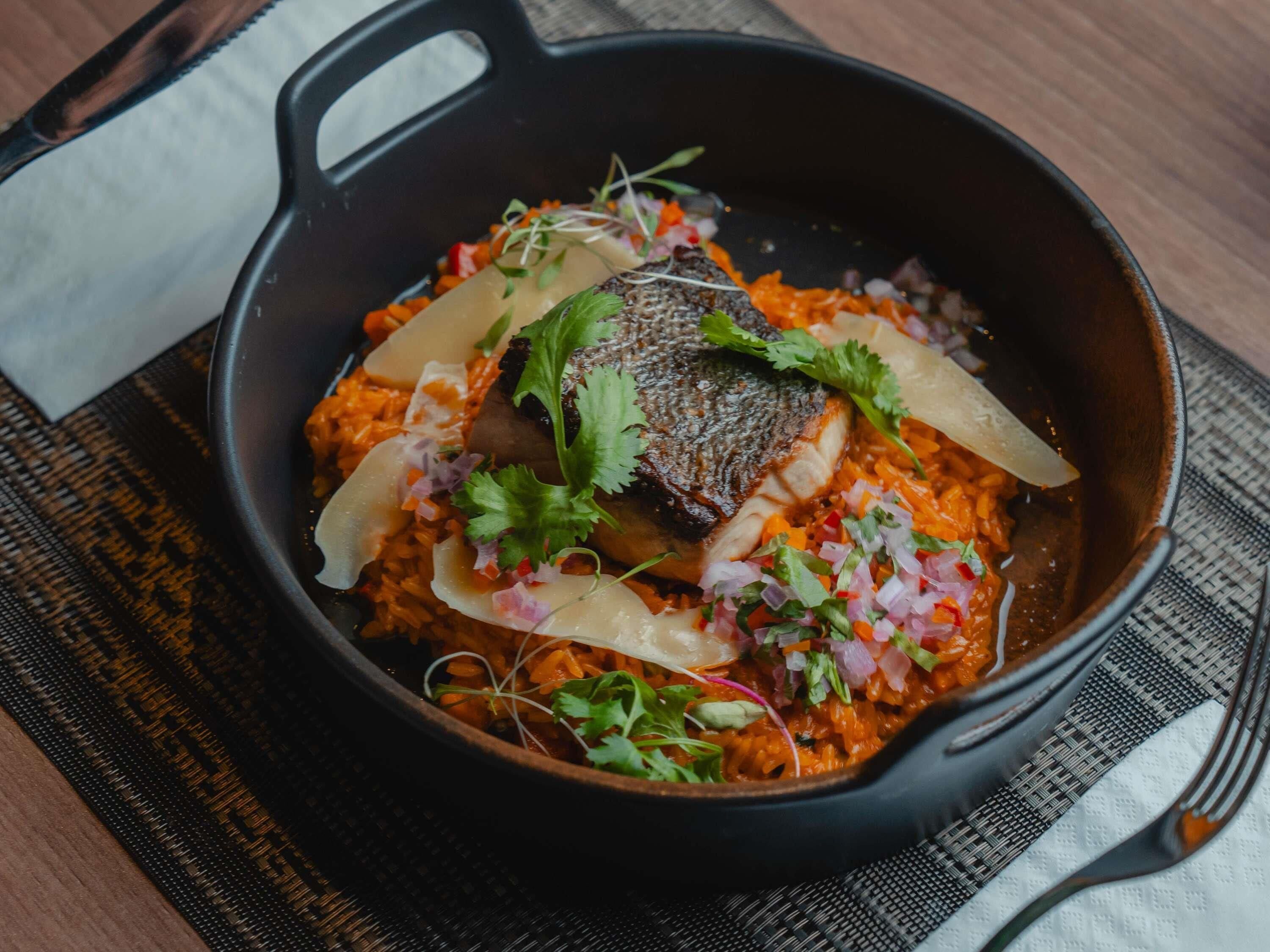 A black cast iron skillet with a meal, including a piece of meat, rice, and garnishes.