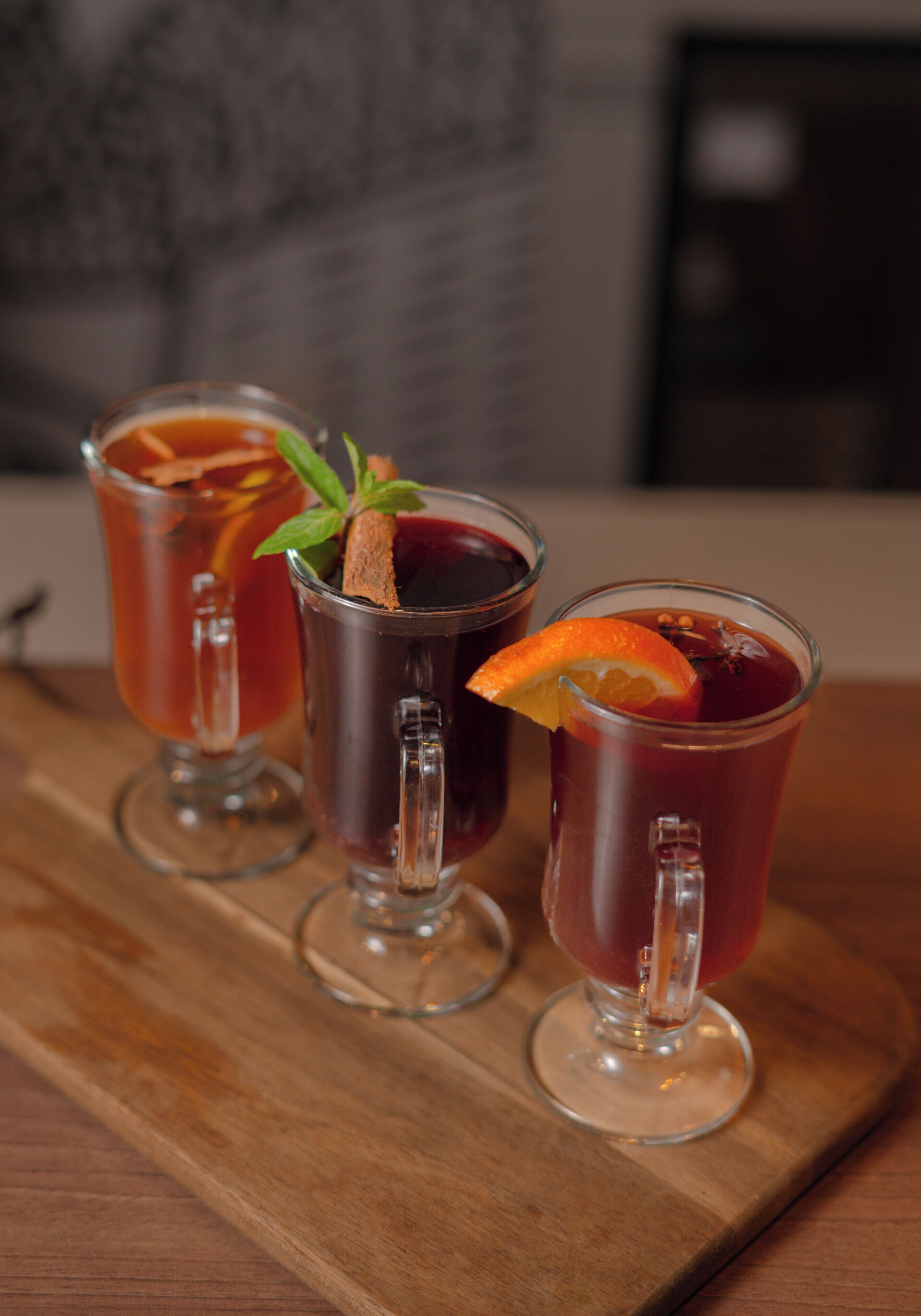 Three glasses of red beverage on a wooden tray.