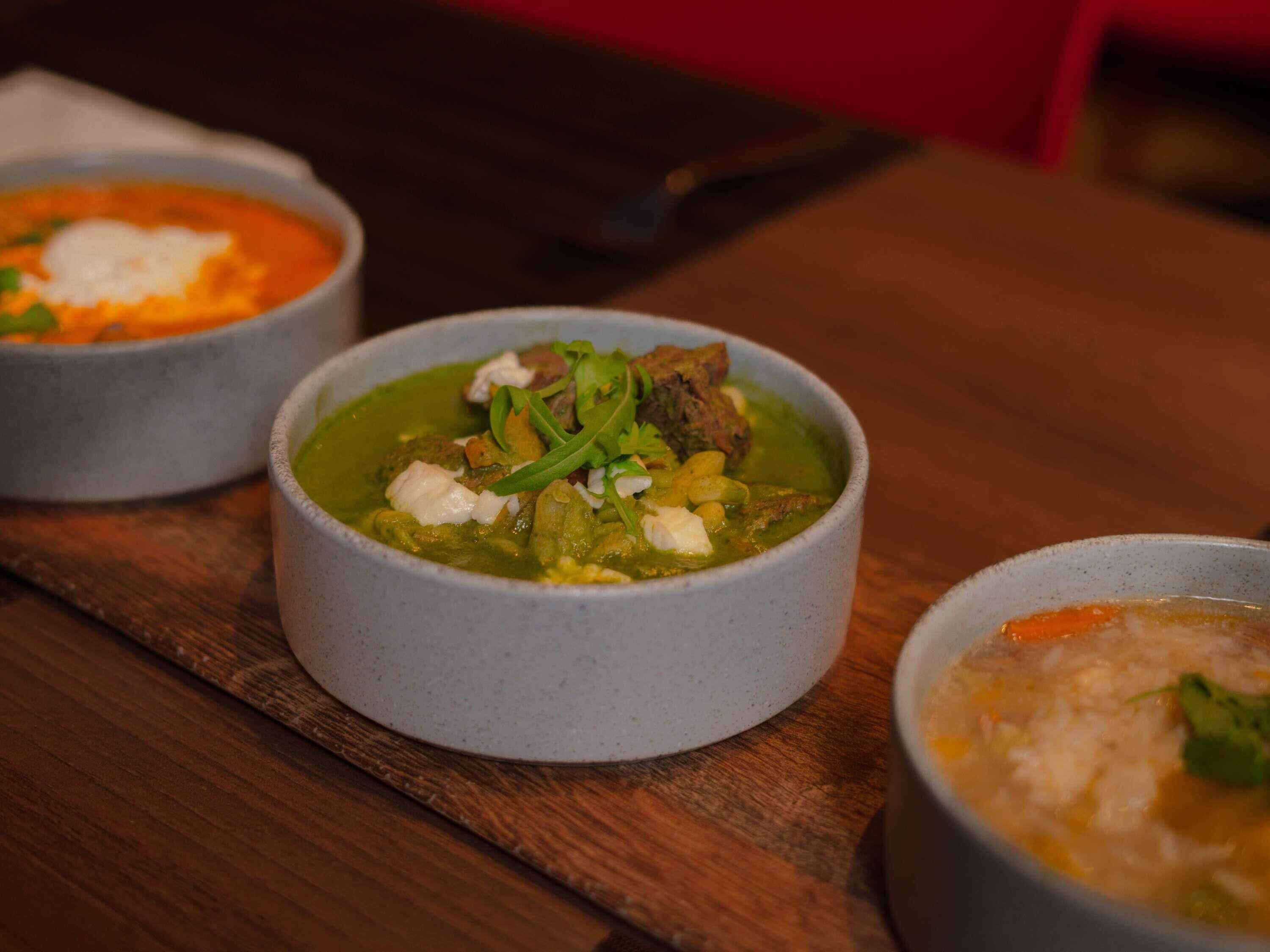 Three bowls of soup on a wooden table.