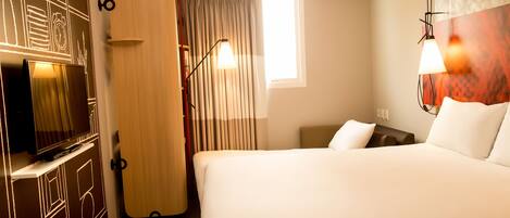 Una habitación de hotel con una cama, televisión, escritorio, lámpara y ventana.