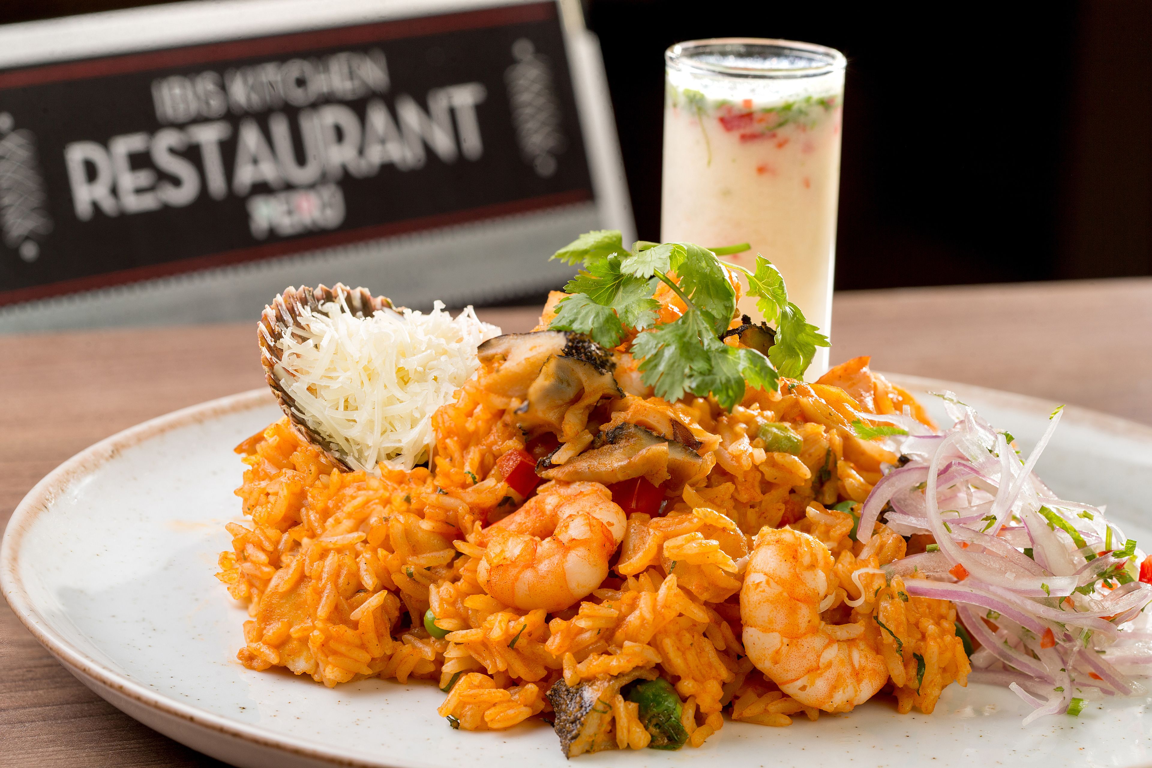 A plate of shrimp and rice with a side salad and a glass of beverage.