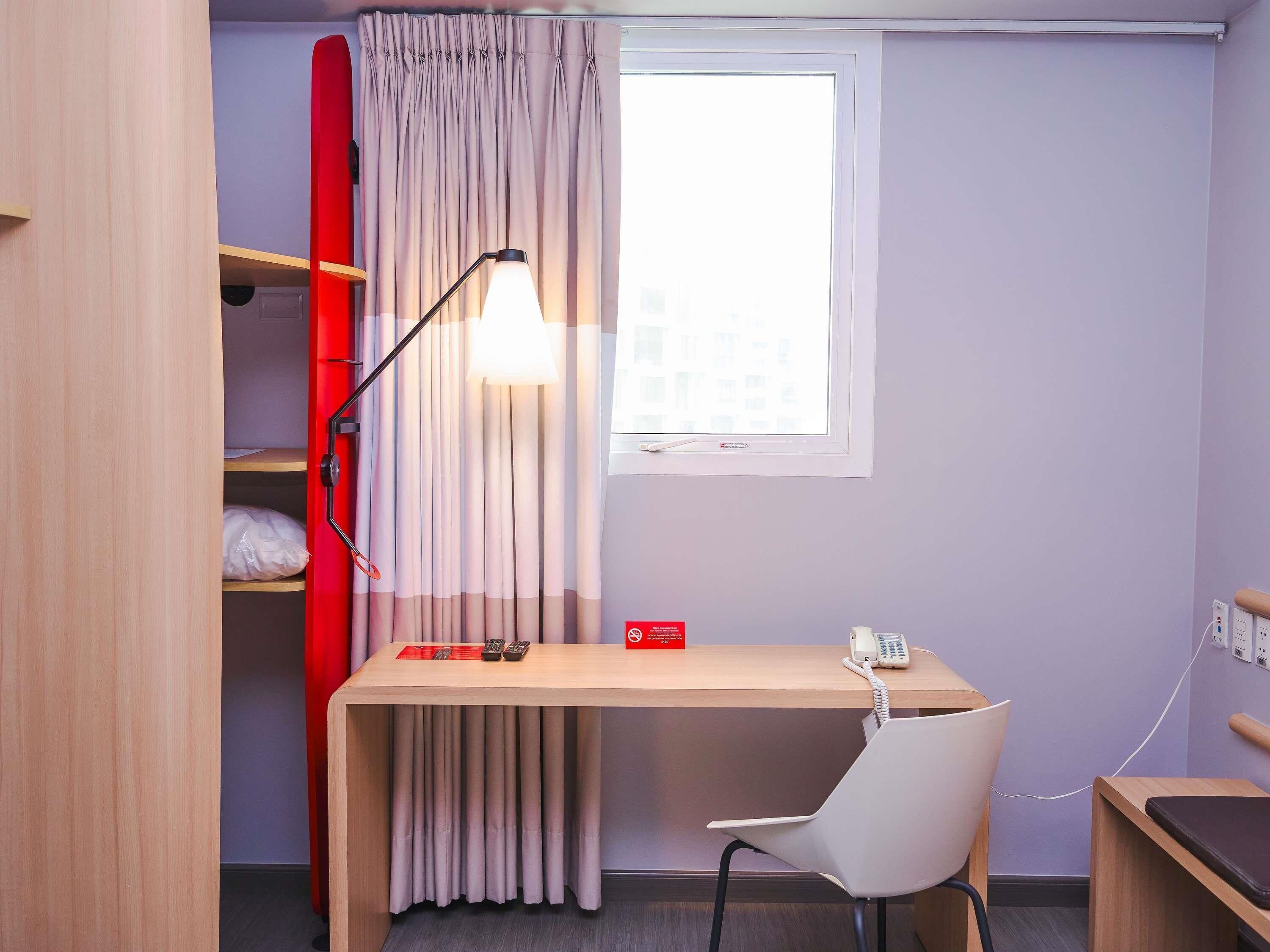 Habitación pequeña con escritorio, silla y ventana con cortinas.