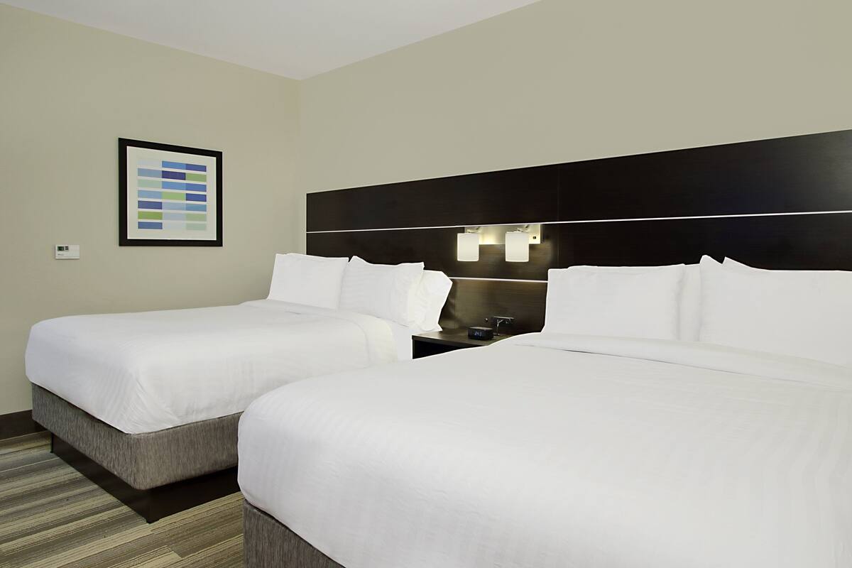 A hotel room with two beds, a framed picture on the wall, and a nightstand with a lamp.