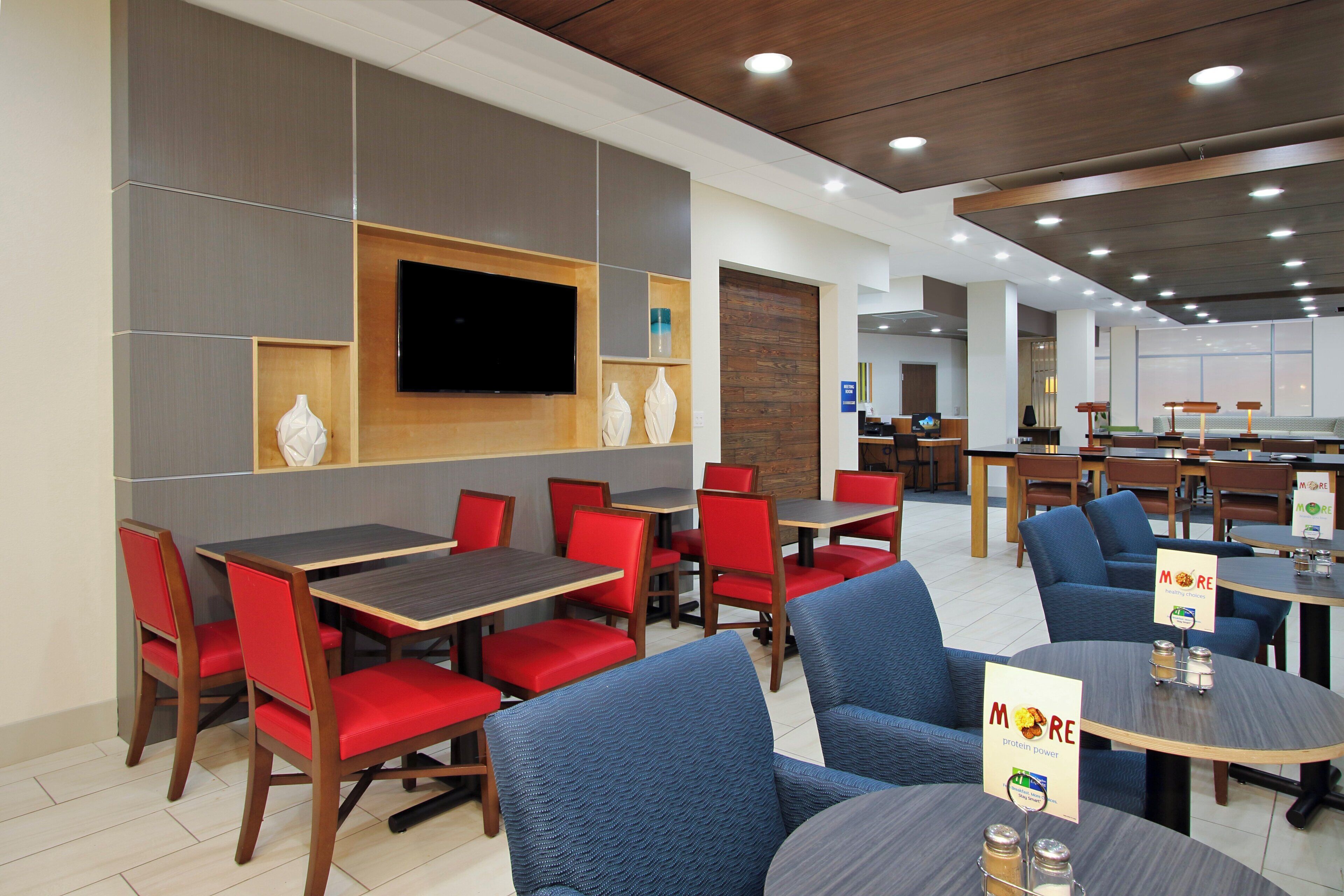 A modern restaurant with red and blue seating, a flat-screen TV, and a sign indicating healthy choices.