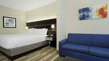 A hotel room with a bed, a blue sofa, a nightstand with a phone, and a geometric wall art piece.
