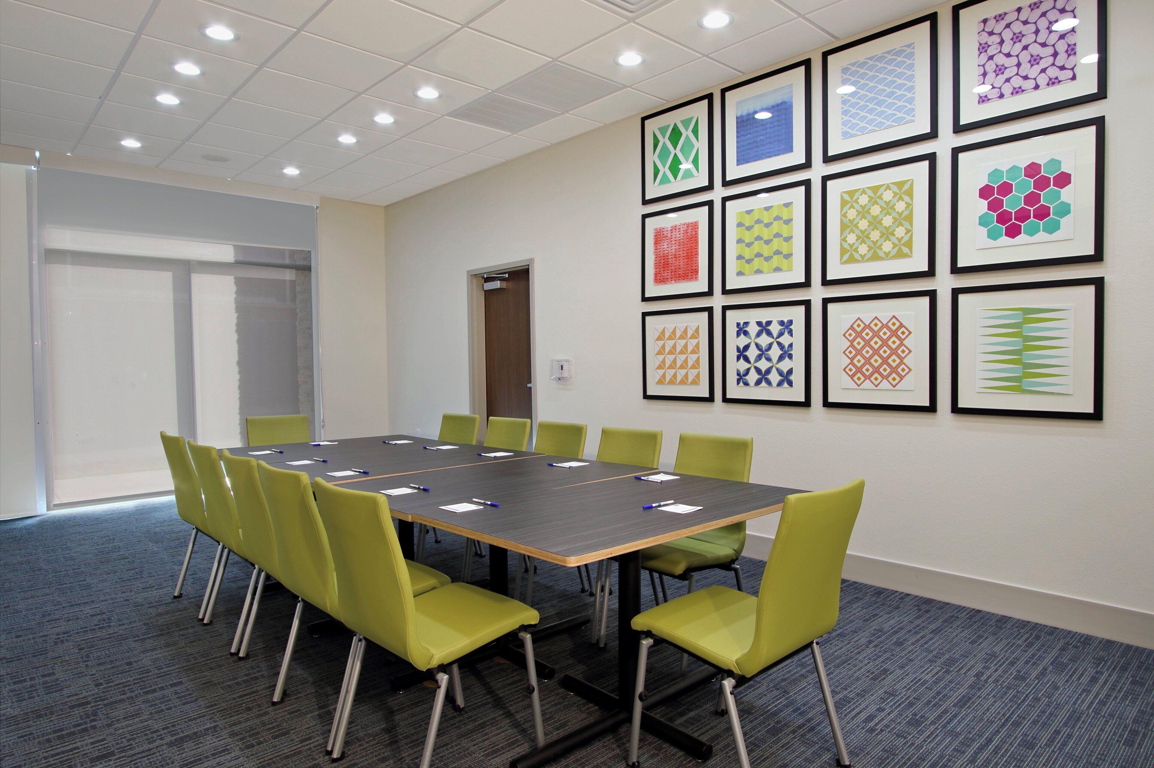 Uma sala de conferências com uma mesa comprida, cadeiras verdes e quadros nas paredes.