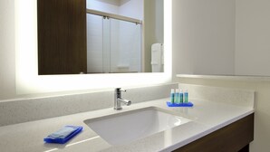 Un baño con un lavamanos blanco, un espejo y artículos de aseo en la encimera.