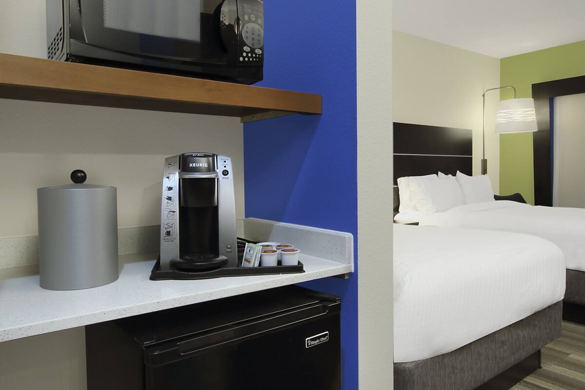 A hotel room with a bed, a coffee machine, a microwave, and a trash bin.