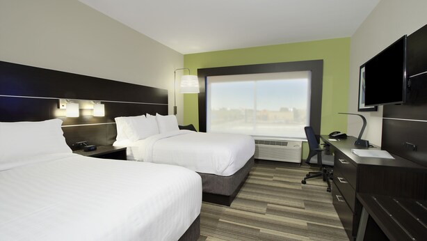 Habitación de hotel con dos camas, un escritorio, una silla, un televisor y un ventanal con vistas a la ciudad.