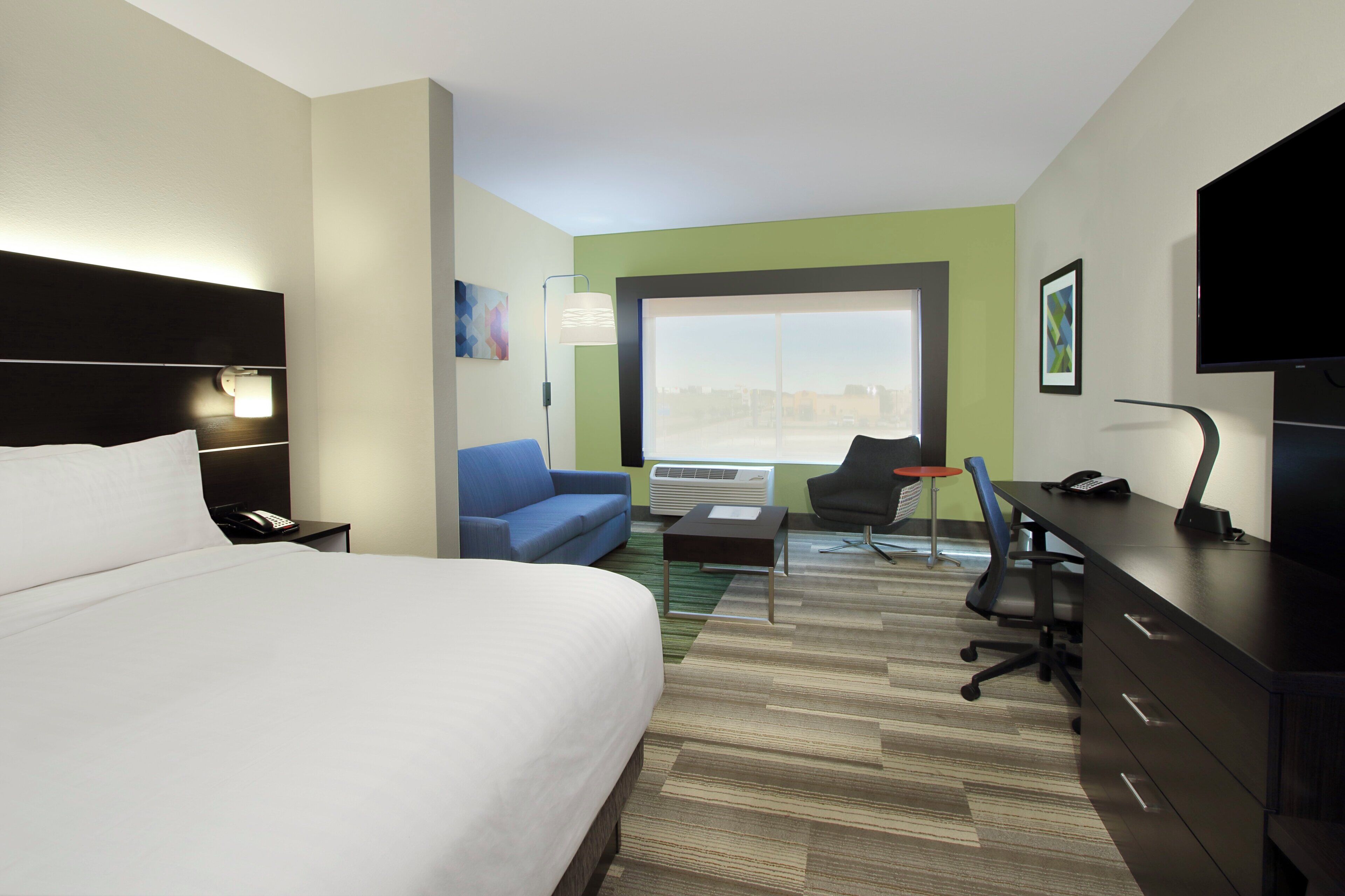 A hotel room with a bed, a desk, a chair, a sofa, and a television.