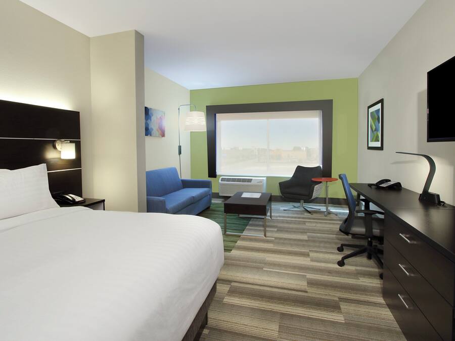 A hotel room with a bed, a desk, a chair, a sofa, and a television.
